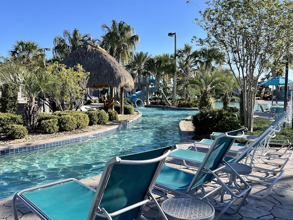 A pool area with lounge chairs, a thatched-roof structure, and palm trees.