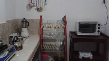 Una cocina con tetera, licuadora, tostadora y un escurridor con tazas y cuencos.
