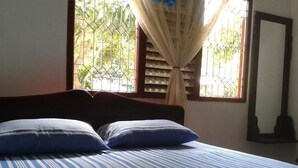 Una cama con ropa de cama a rayas, una ventana con cortina y un espejo en la pared.