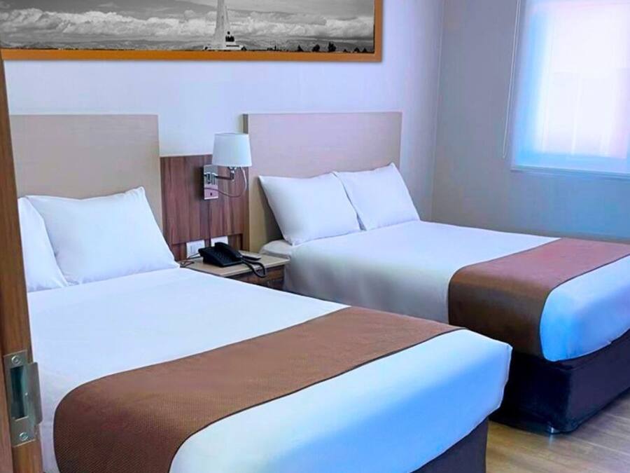 Una habitación de hotel con dos camas, una mesita de noche con lámpara y un cuadro en la pared.