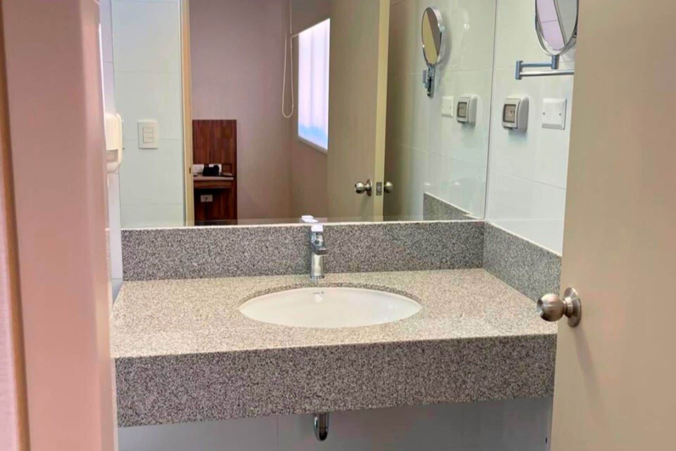 A bathroom with a granite countertop sink, a mirror, and a door leading to another room.