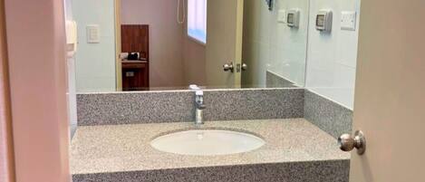 Baño con lavamanos de encimera de granito, espejo y puerta que da a otra habitación.