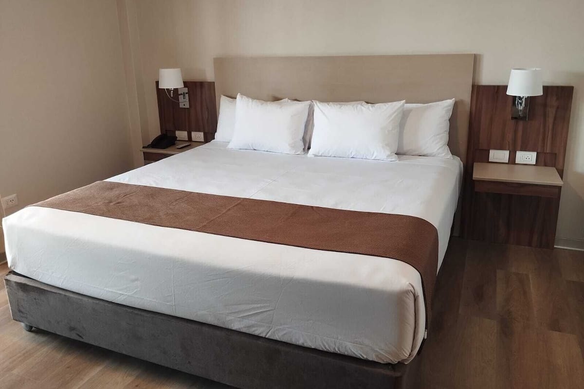 A large bed with a wooden headboard, white bedding, and two bedside tables with lamps.