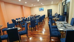 Un salón de conferencias con filas de sillas azules y mesas, una pantalla de televisión en la pared y un suelo de madera pulida.