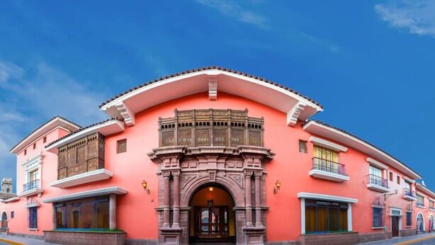 Un edificio rosa con un arco central, balcones y un cielo azul claro.