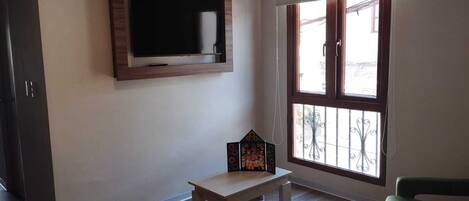 Una sala de estar con un televisor de pantalla plana montado en la pared, una pequeña mesa de madera y un sillón verde.