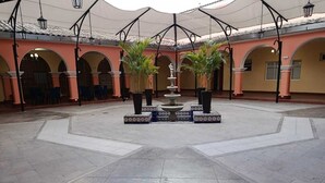 Un patio amplio con una fuente central, rodeado de arcos y plantas en macetas.