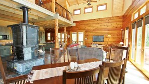 A spacious log cabin interior with a stone fireplace, wooden dining table, and a balcony overlooking the yard. - Ashling Ranch - Gorgeous, luxury log home with access to Yellowstone River! (Emigrant)