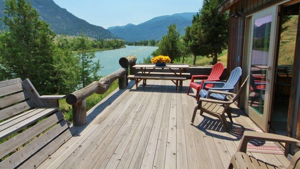 A wooden deck with a river view, picnic table, and Adirondack chairs. - Ashling Ranch - Gorgeous, luxury log home with access to Yellowstone River! (Emigrant)
