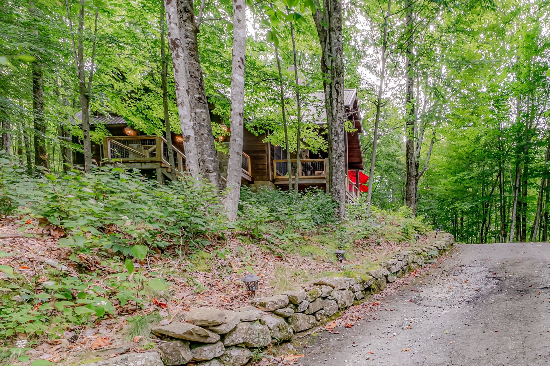 A rustic cabin with a stone wall and wooden deck, surrounded by dense forest.