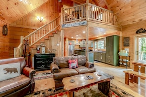 A wooden cabin interior with a living area, a kitchen, and a staircase.