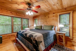 A wooden cabin bedroom with a bed, a nightstand, a lamp, and a ceiling fan.