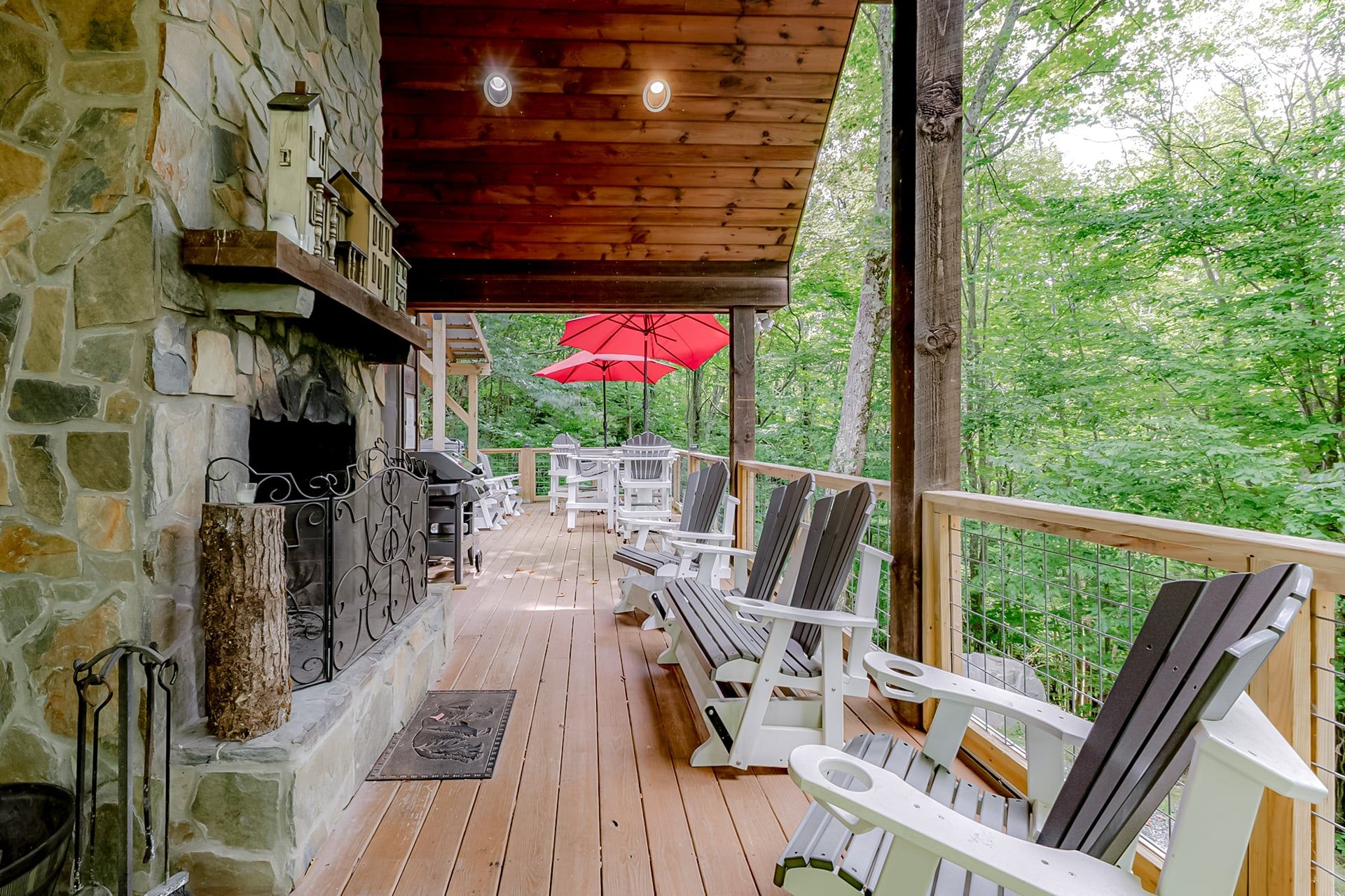 A wooden deck with Adirondack chairs, a stone fireplace, and a red umbrella.