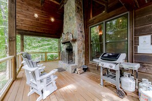 A wooden deck with a stone fireplace, a grill, and outdoor seating.