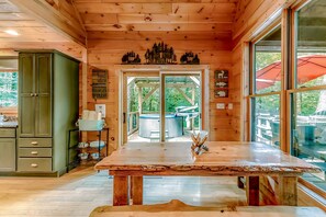 A wooden cabin interior with a dining table, a hot tub, and a view of the outdoors.