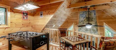 A wooden interior with a foosball table, a chess table, and a ceiling fan.