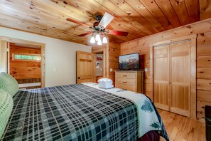A wooden cabin room with a bed, a television, and a ceiling fan.