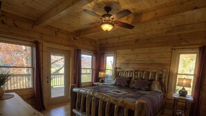 Ein Schlafzimmer einer Holzhütte mit Bett, Deckenventilator und großen Fenstern.