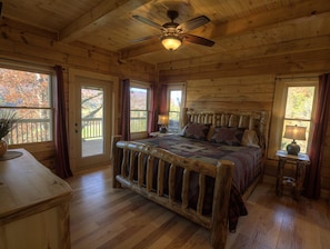 Une chambre dans une cabane en bois, avec un lit, un ventilateur de plafond et de grandes fenêtres.
