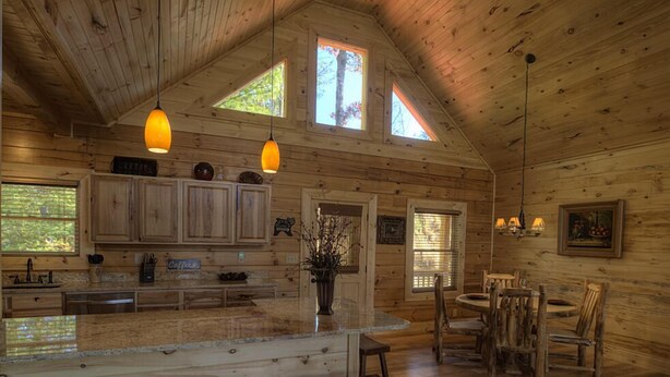 Ein rustikales Blockhaus-Interieur mit Holzwänden, einer Küchenzeile, einem Esstisch mit Stühlen und einer Bar mit Hockern.