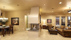 A spacious living room with a fireplace, a dining area with a chandelier, and a cozy seating area with a sofa and armchairs. - Golf & Baseball Batting Cage/ Hot Tub/ Luxurious Living/ Private, Gated, Quiet (Scottsdale)