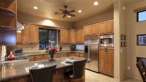 A modern kitchen with wooden cabinets, a stainless steel refrigerator, and a central island with bar stools. - Golf & Baseball Batting Cage/ Hot Tub/ Luxurious Living/ Private, Gated, Quiet (Scottsdale)