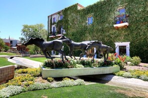 Un jardin agrémenté d’une statue de cheval, entouré de parterres de fleurs bien entretenus et d’un chemin pavé.