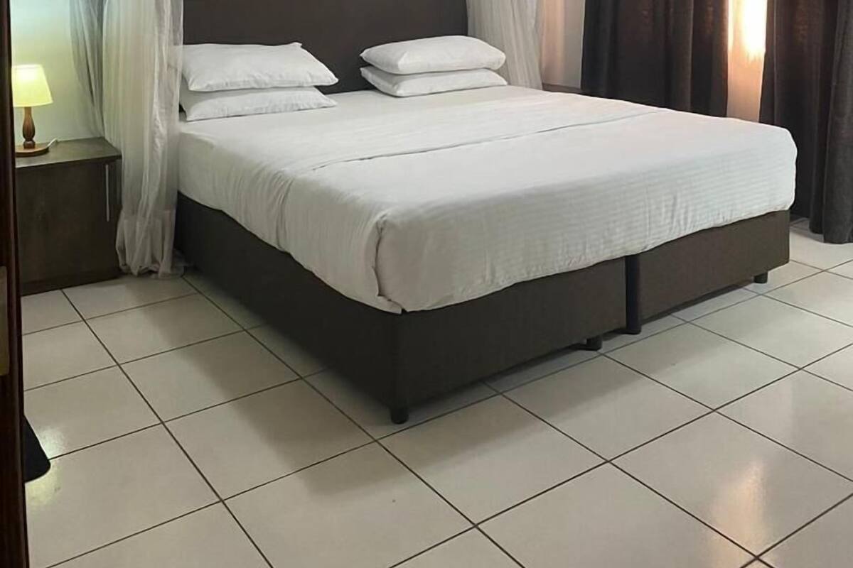 A neatly made bed with white linens, a headboard, and a nightstand with a lamp.