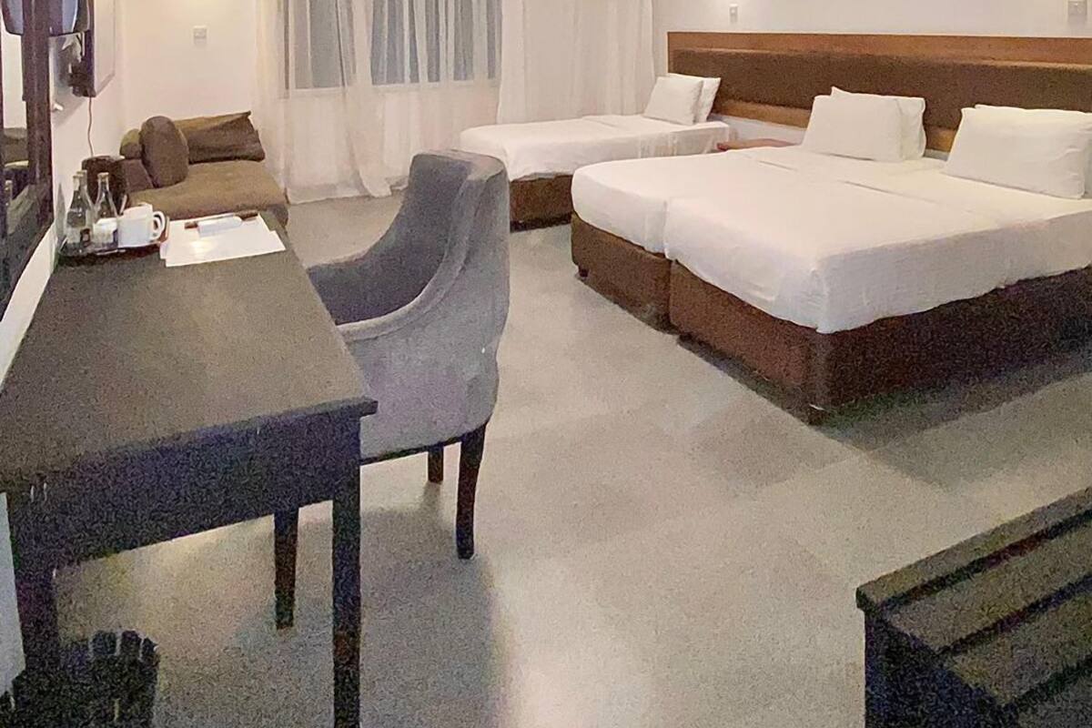 A hotel room with two single beds, a desk, a chair, a TV, and a window with curtains.