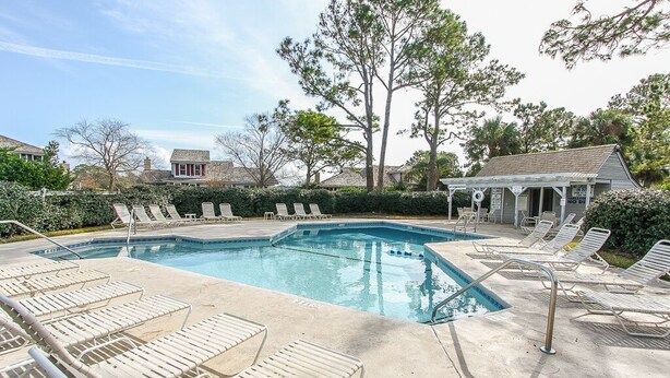 A swimming pool with lounge chairs, a small building, and trees in the background. - Beautiful Lands End Townhome with Spectacular Water Views & Close to Beach (Hilton Head Island)