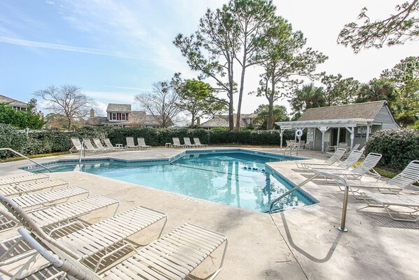 A swimming pool with lounge chairs, a small building, and trees in the background.