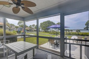 A covered outdoor area with a table and chairs, overlooking a grassy area and a body of water.