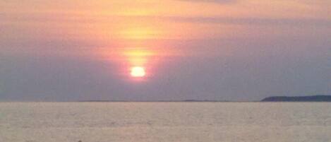 Un coucher de soleil sur une mer calme, avec une terre lointaine à l'horizon.