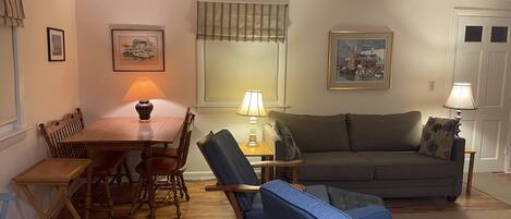 A cozy living room with a wooden dining table, blue chairs, a grey sofa, and two lamps.