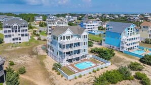 A coastal residential area with multi-story houses featuring balconies and a swimming pool. - Premier Dog-Friendly Oceanfront 9BR w/ Private Pool, Tiki Bar, Theater, Elevator (Salvo)