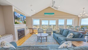 A spacious living room with a fireplace, a large sofa, a coffee table, and a view of the ocean through large windows. - Premier Dog-Friendly Oceanfront 9BR w/ Private Pool, Tiki Bar, Theater, Elevator (Salvo)
