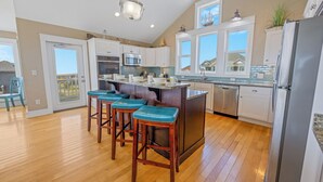 A modern kitchen with a central island, bar stools, stainless steel appliances, and large windows. - Premier Dog-Friendly Oceanfront 9BR w/ Private Pool, Tiki Bar, Theater, Elevator (Salvo)