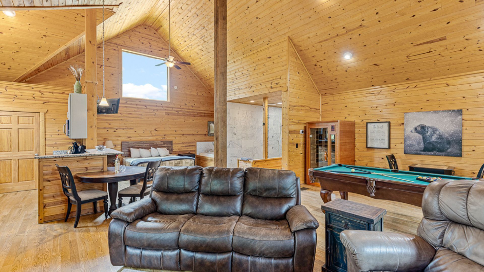 Un intérieur de chalet chaleureux avec un coin repas, un canapé, une table de billard et une grande fenêtre.