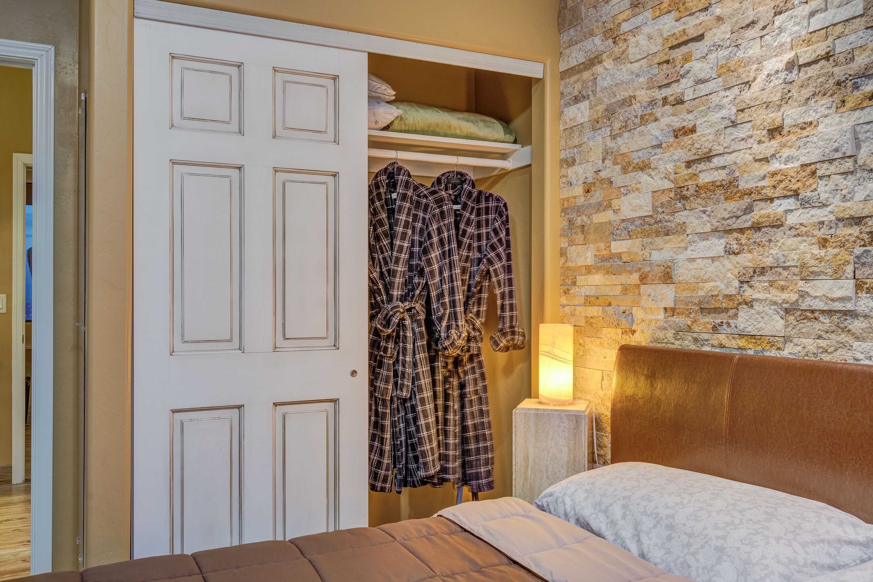 Une chambre à coucher avec un lit, une armoire remplie de vêtements, un mur en briques et une table de chevet avec une lampe.