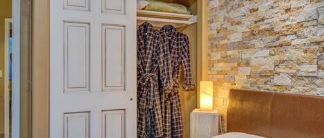 Une chambre à coucher avec un lit, une armoire remplie de vêtements, un mur en briques et une table de chevet avec une lampe.