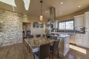 A modern kitchen with a granite island, white cabinets, and a cityscape painting. - New HILLTOP CASITA in the Foothills with surrounding Mountain and City Views!  (Tucson)