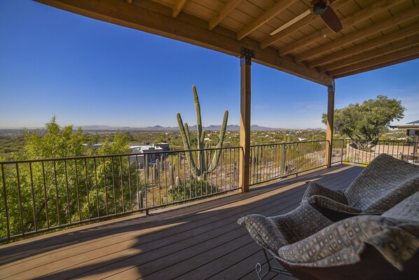 Una terraza de madera con mobiliario exterior, barandilla metálica y vistas a cactus y montañas distantes.