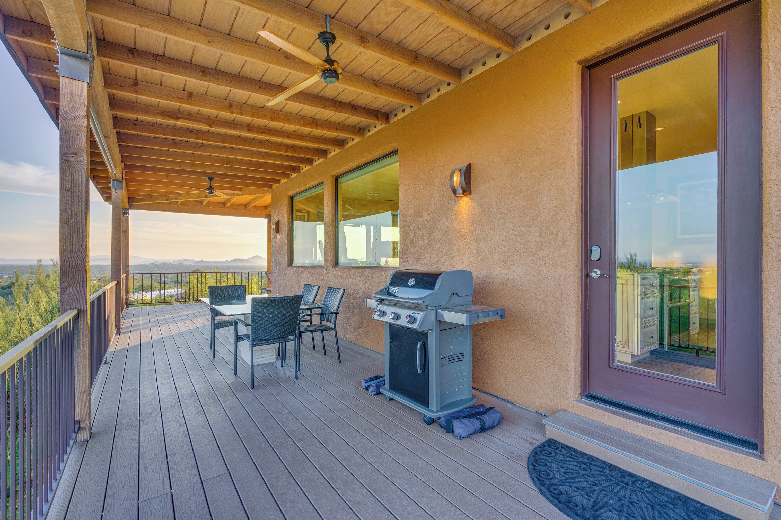 A covered outdoor deck with a grill, chairs, and a table.
