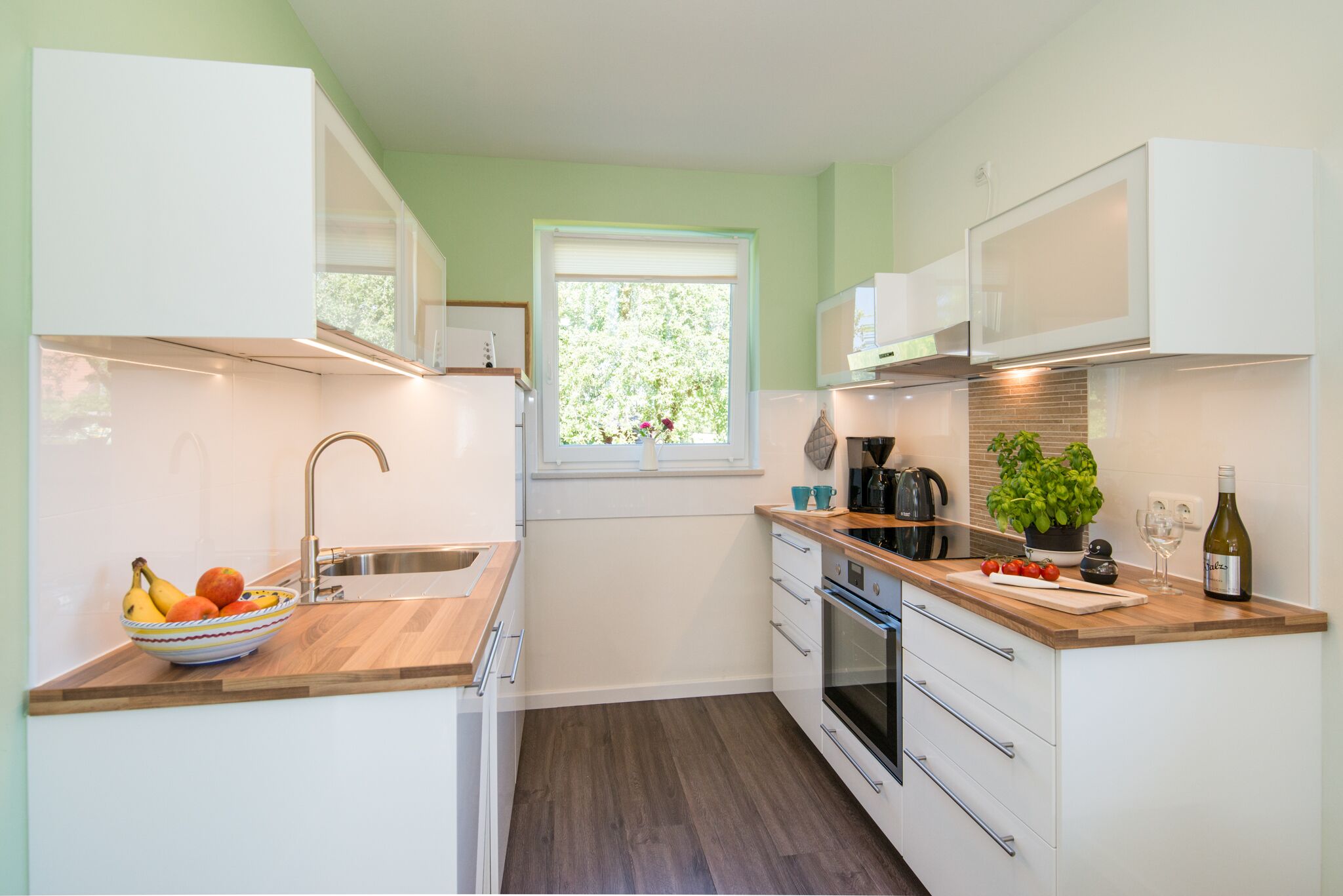 A modern kitchen with white cabinets, a wooden countertop, a sink, a window, and a potted plant.