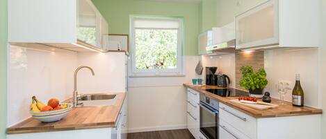 A modern kitchen with white cabinets, a wooden countertop, a sink, a window, and a potted plant.
