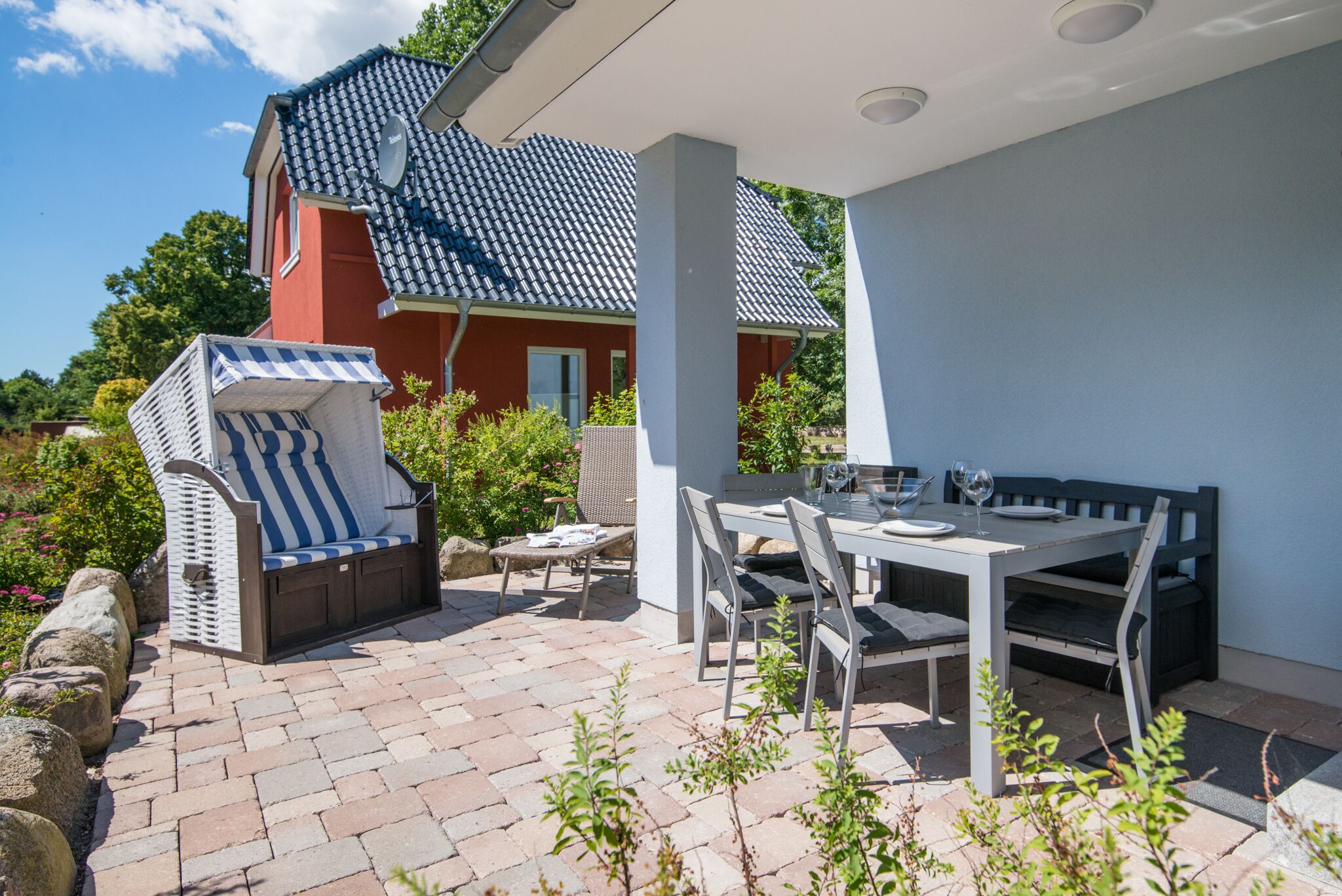 A patio area with a dining table, chairs, a striped sofa, and a small table with a glass.