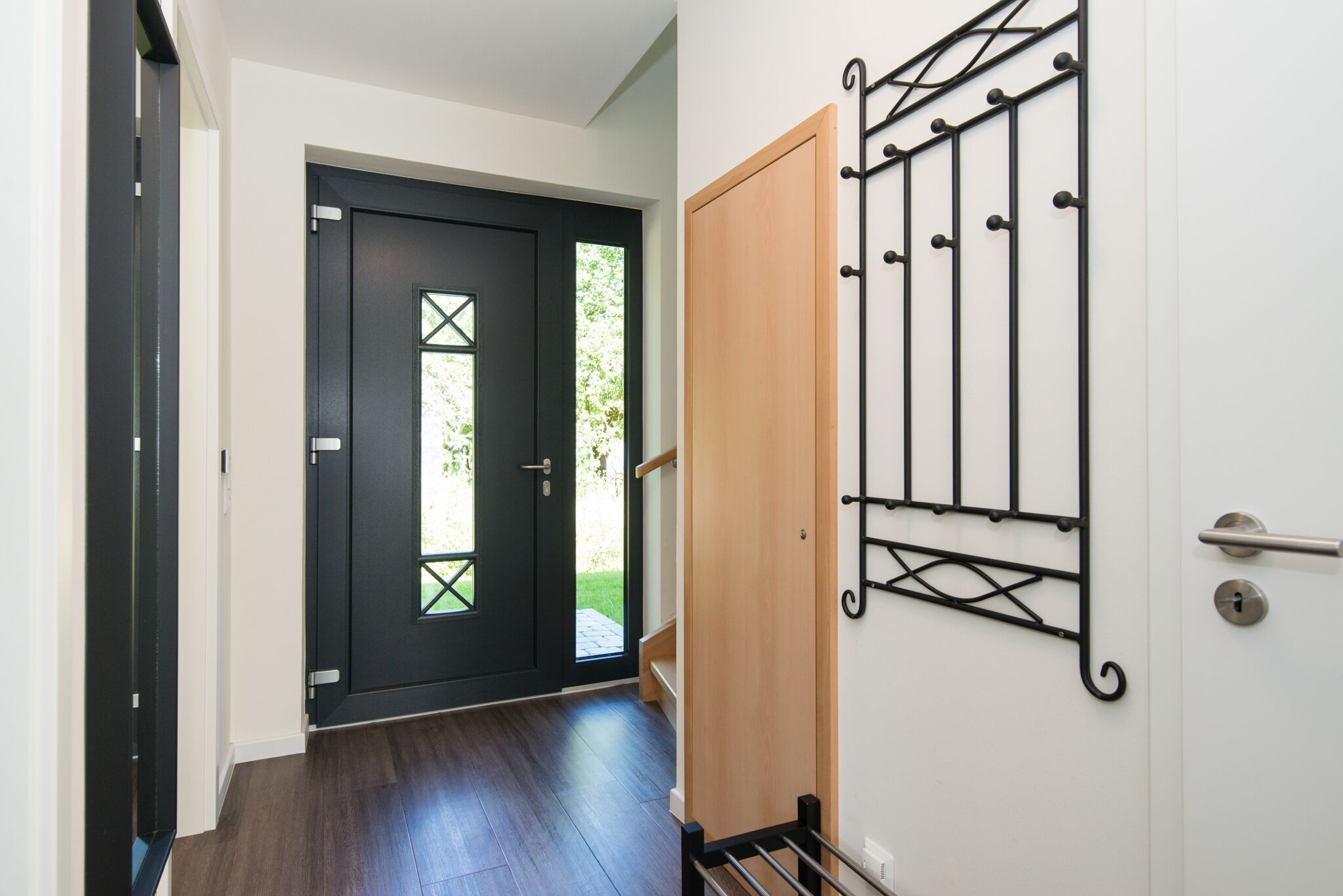 A hallway with a dark wooden door, a light-colored wall with a metal rack, and a wooden door frame.