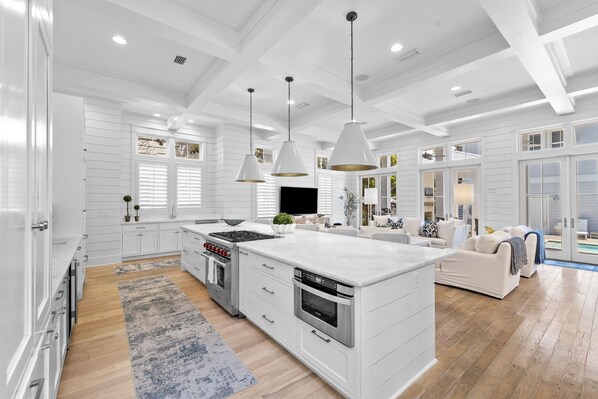 A spacious kitchen with white cabinetry, a central island, stainless steel appliances, pendant lighting, and a large window providing natural light. - WaterColor Luxury on 30A! 63 Western Lake, Park District, Pool, 7 Bdrms, Slps 16+ (Santa Rosa Beach)