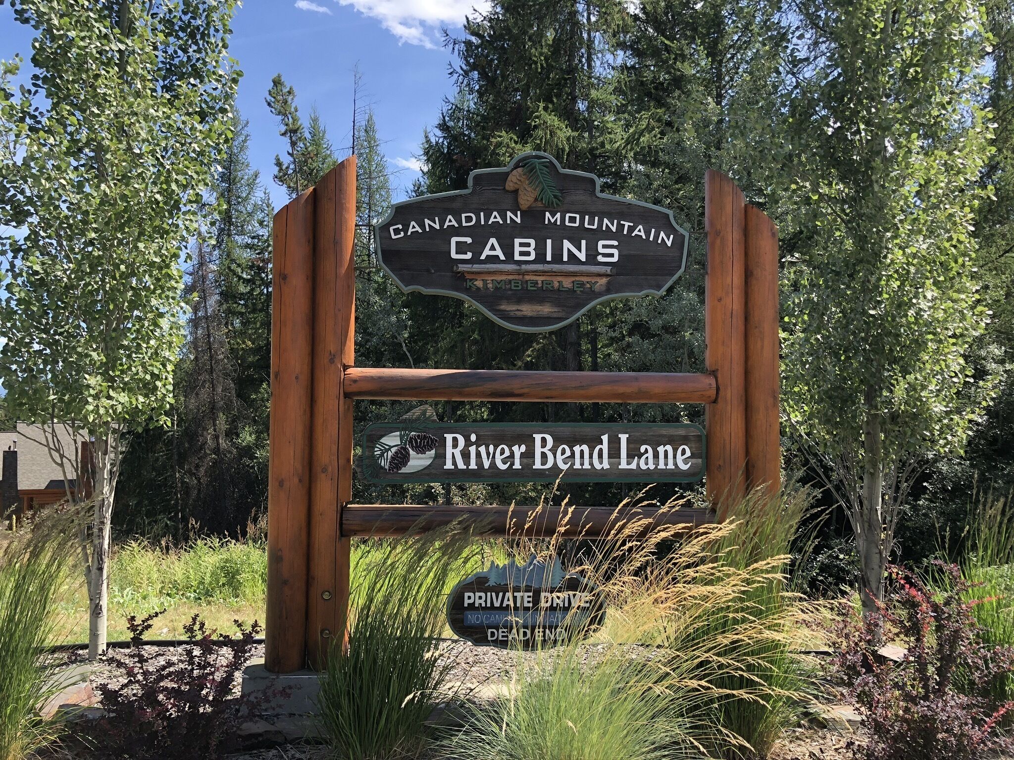 A wooden sign for Canadian Mountain Cabins with a label for River Bend Lane.
