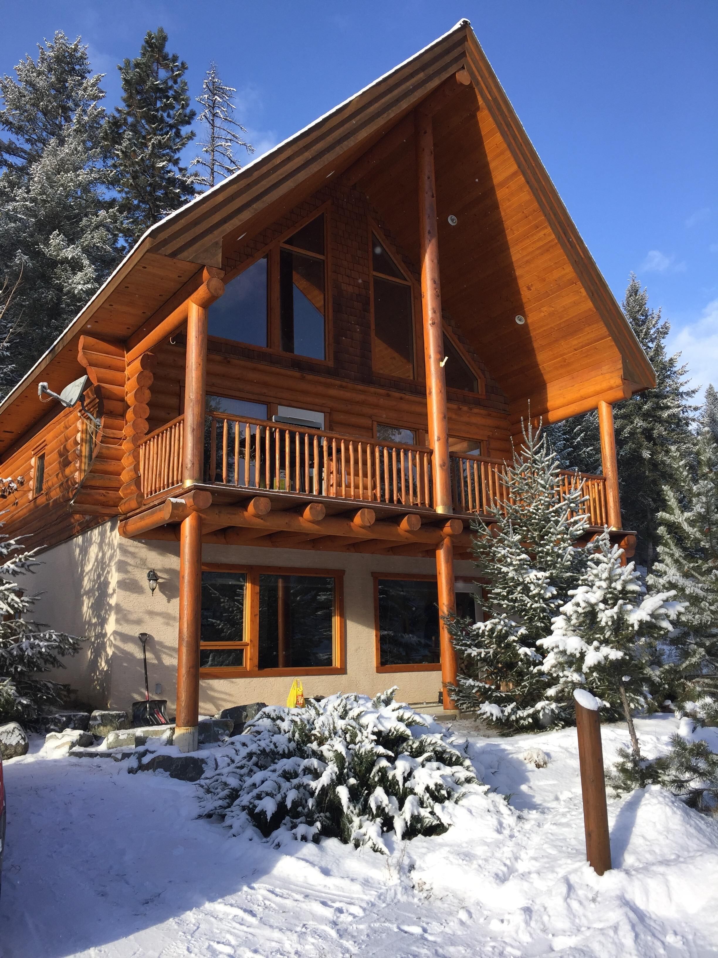 Une cabane en rondins dotée d’un balcon, entourée d’arbres couverts de neige.